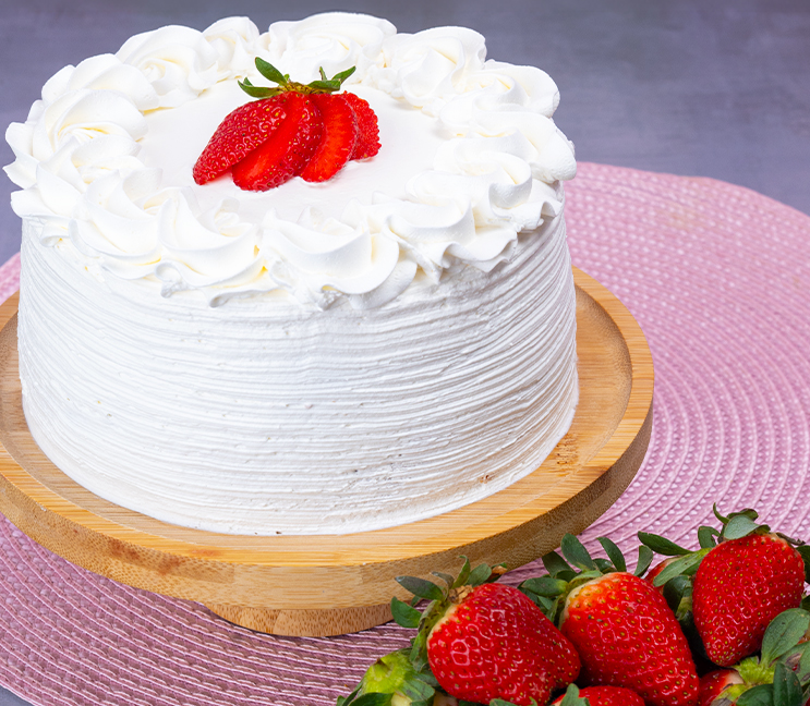 Bolo coberto de chantilly com morangos sobre tábua de madeira